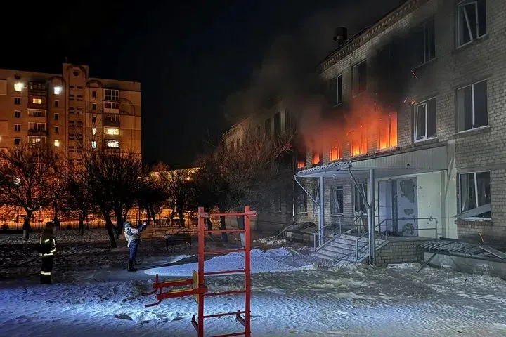 A building burns at night in Kharkiv after a Russian strike as firefighters respond.