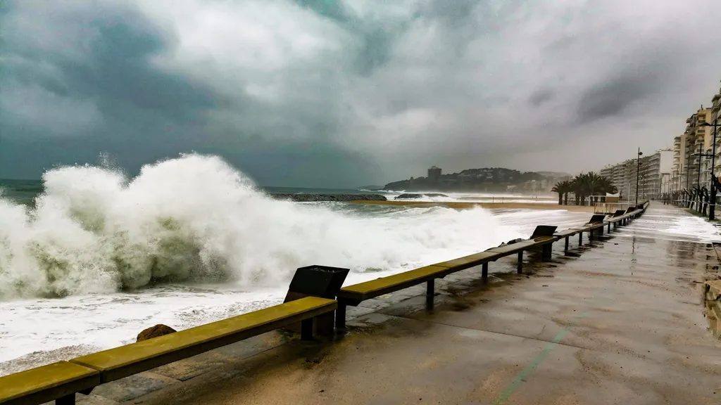 Huge waves crash over a Catalan coastal promenade under storm clouds