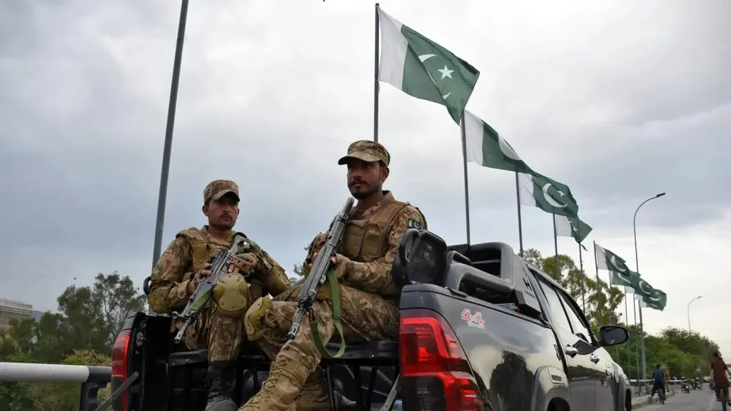 Pakistani soldiers with rifles in a pickup under Pakistani flags