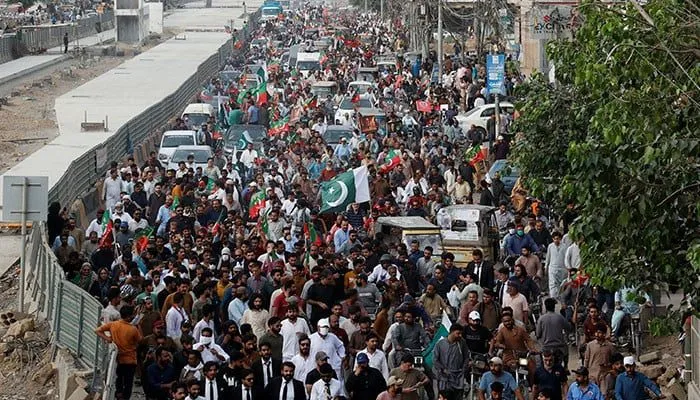 Thousands of PTI supporters march with party flags through a city street