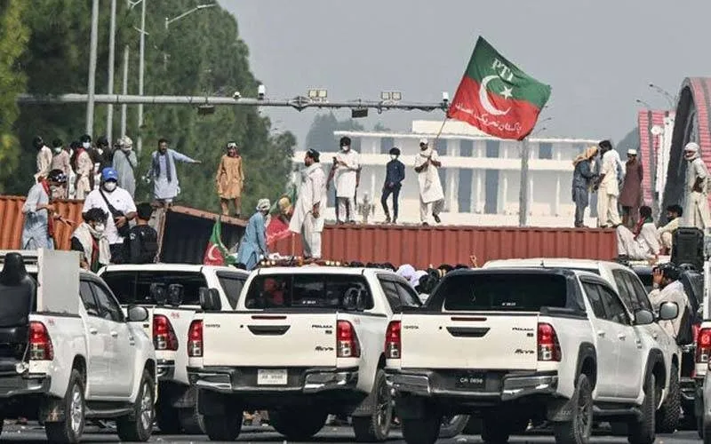 PTI supporters wave a party flag atop shipping containers blocking a march route