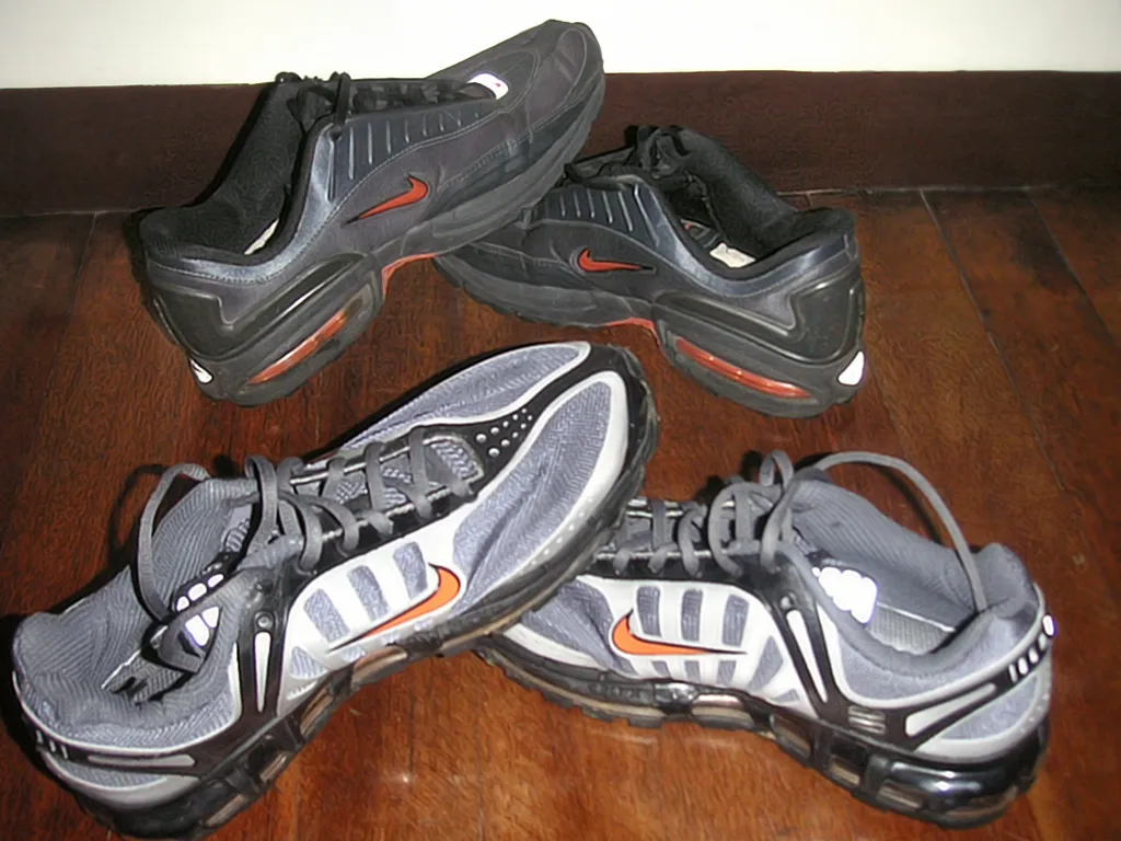 Two pairs of Nike Air Max trainers with orange swoosh logos on a wooden floor